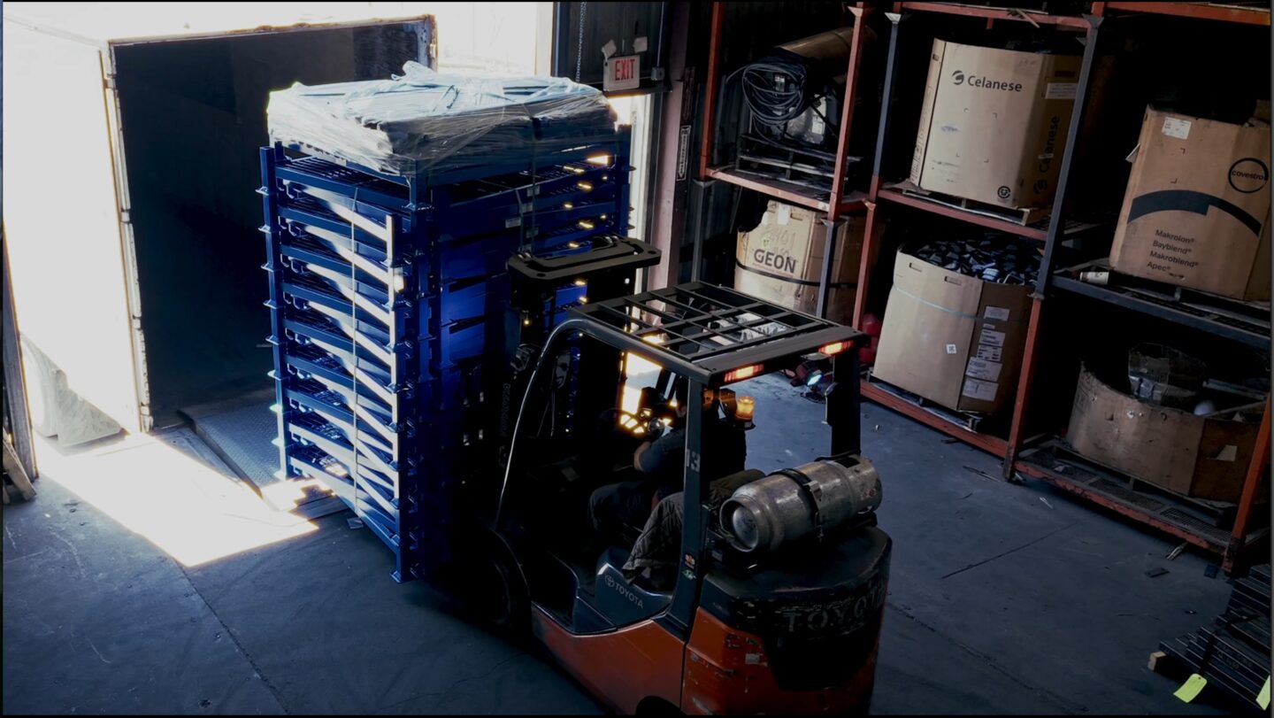 Forklift moving stacked blue racks for shipment from an Ohio Rack facility.